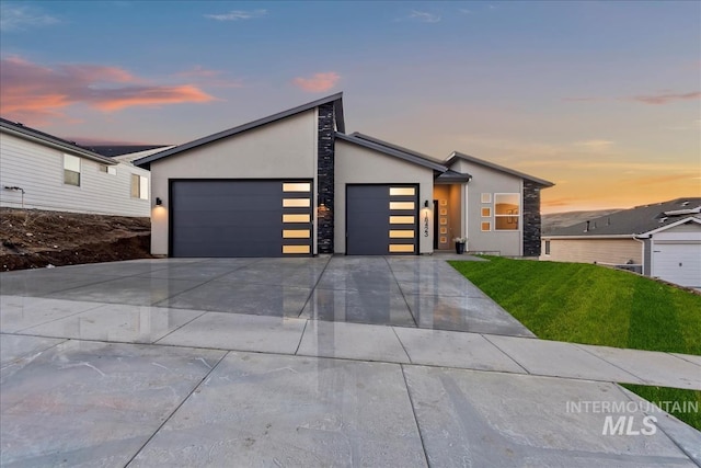 contemporary home with a garage, concrete driveway, stone siding, a front lawn, and stucco siding