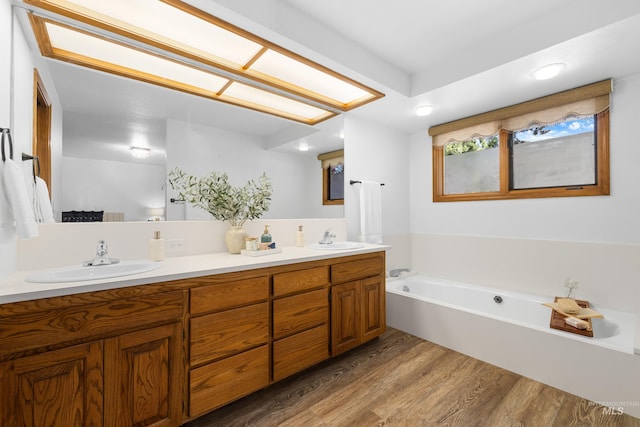bathroom featuring a garden tub, wood finished floors, a sink, and double vanity