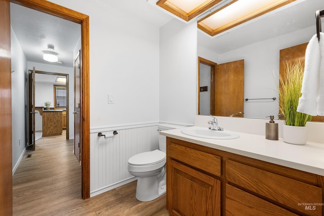 half bathroom featuring vanity, toilet, a wainscoted wall, and wood finished floors