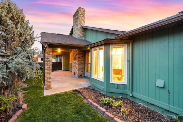 back of property at dusk with a chimney, a patio, and a lawn