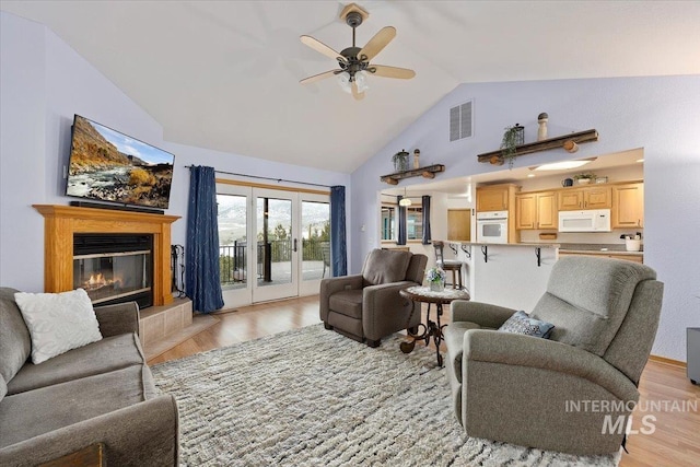 living area featuring french doors, visible vents, a ceiling fan, light wood-type flooring, and a tile fireplace