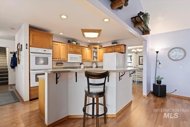 kitchen with light wood-type flooring, white appliances, and a breakfast bar area