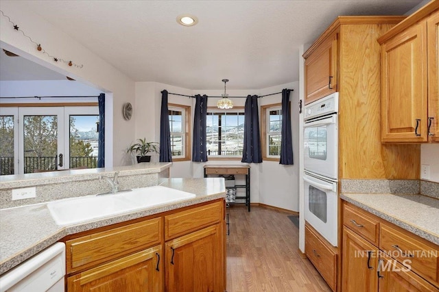 kitchen with brown cabinets, light countertops, light wood-style floors, a sink, and white appliances