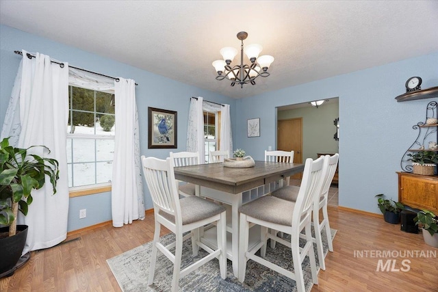 dining space featuring a chandelier, a textured ceiling, light wood-style flooring, and baseboards