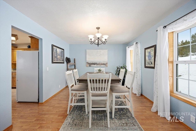 dining area with a chandelier, light wood-type flooring, a textured ceiling, and baseboards