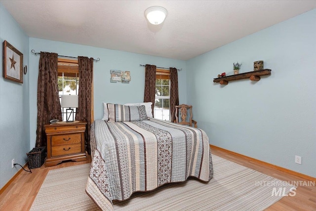 bedroom with a textured ceiling, wood finished floors, and baseboards