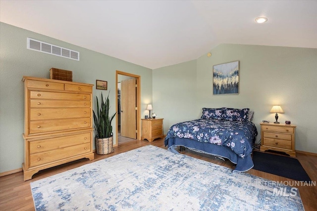 bedroom with lofted ceiling, wood finished floors, visible vents, and baseboards