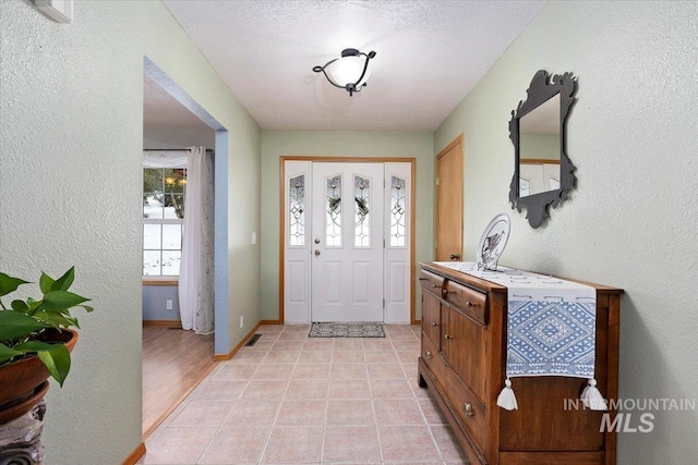 entrance foyer featuring visible vents, a textured wall, light tile patterned flooring, a textured ceiling, and baseboards