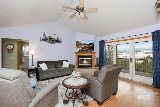 living room with ceiling fan, vaulted ceiling, french doors, light wood-type flooring, and a tiled fireplace