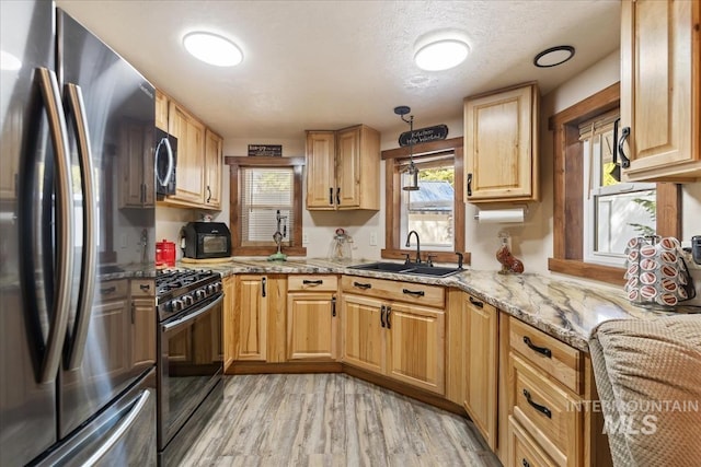 kitchen featuring black range with gas cooktop, light stone countertops, light wood-type flooring, a sink, and freestanding refrigerator