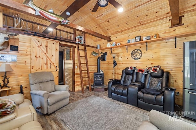 living room featuring ceiling fan, a wood stove, wood finished floors, lofted ceiling with beams, and wooden walls