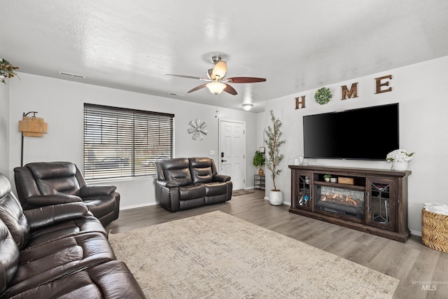 living room with ceiling fan, wood finished floors, baseboards, and a glass covered fireplace