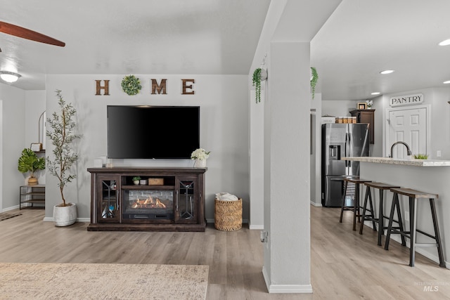 living room featuring light wood-style flooring, baseboards, a ceiling fan, a multi sided fireplace, and recessed lighting