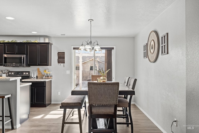 dining space featuring light wood-type flooring, a chandelier, baseboards, a textured wall, and recessed lighting