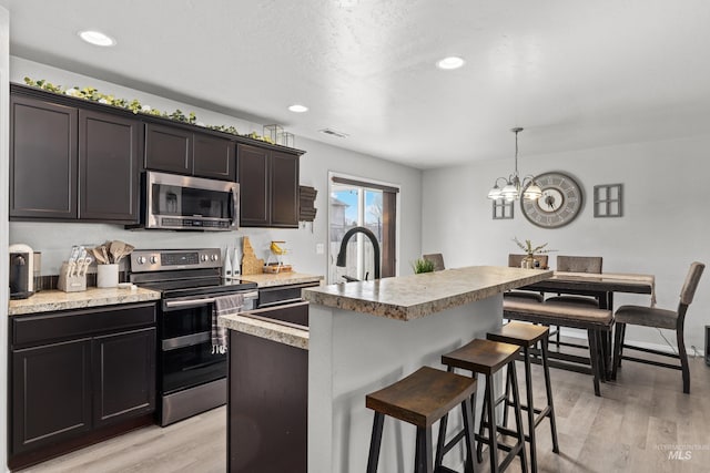 kitchen featuring appliances with stainless steel finishes, a sink, light wood-type flooring, a center island with sink, and a kitchen breakfast bar