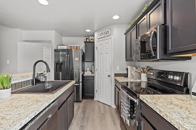 kitchen featuring appliances with stainless steel finishes, a sink, light wood-style flooring, light countertops, and recessed lighting