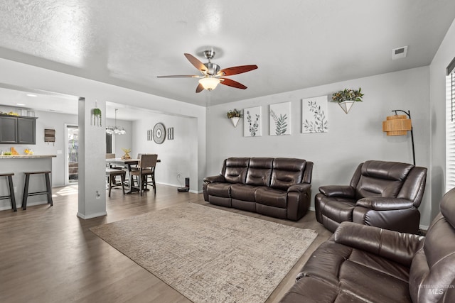 living area with dark wood-type flooring, a ceiling fan, a chandelier, and baseboards
