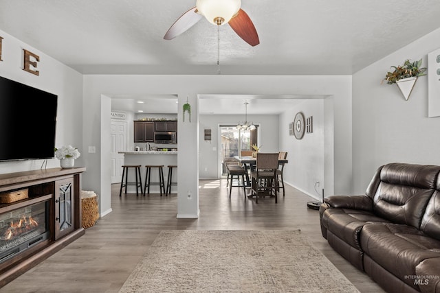 living area featuring a ceiling fan, wood finished floors, baseboards, and a glass covered fireplace