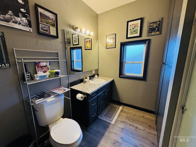 bathroom with baseboards, a textured wall, toilet, wood finished floors, and vanity