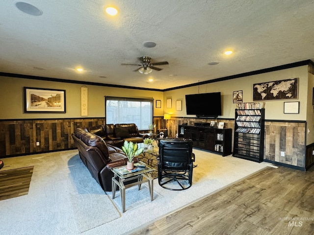 living area with wooden walls, wainscoting, crown molding, and a textured ceiling