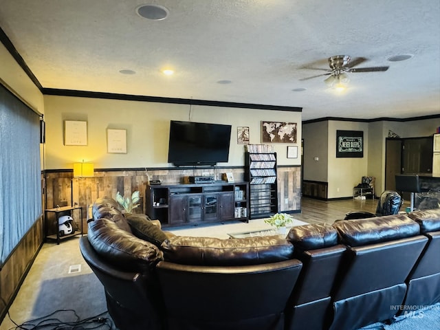 living room featuring wood walls, ornamental molding, a textured ceiling, and wainscoting