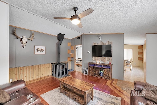 living room with a wood stove, ceiling fan, wood-type flooring, a textured ceiling, and vaulted ceiling