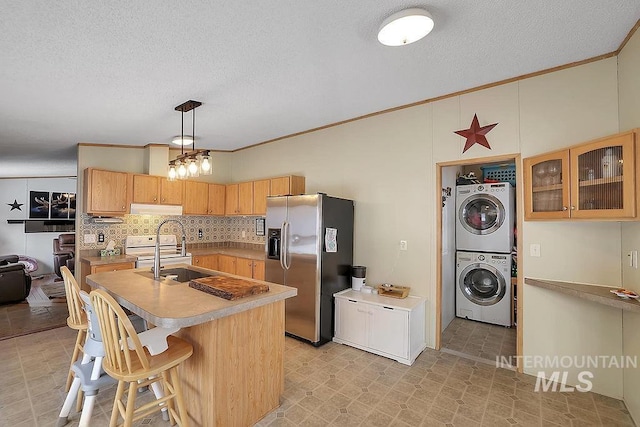 kitchen featuring stainless steel refrigerator with ice dispenser, hanging light fixtures, stacked washing maching and dryer, ornamental molding, and tasteful backsplash