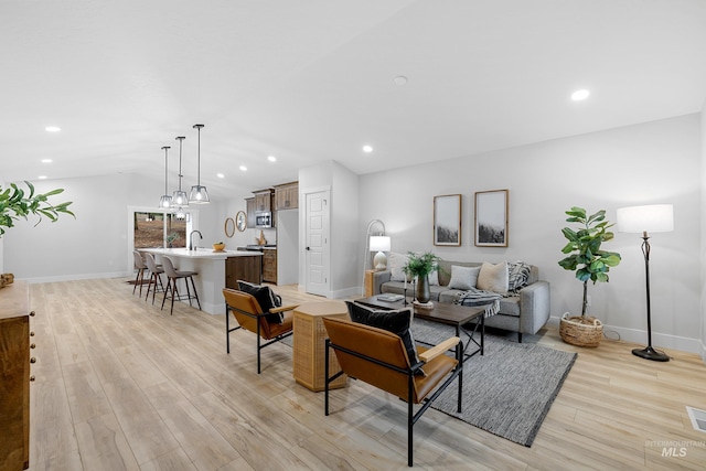 living room with lofted ceiling, sink, and light hardwood / wood-style floors