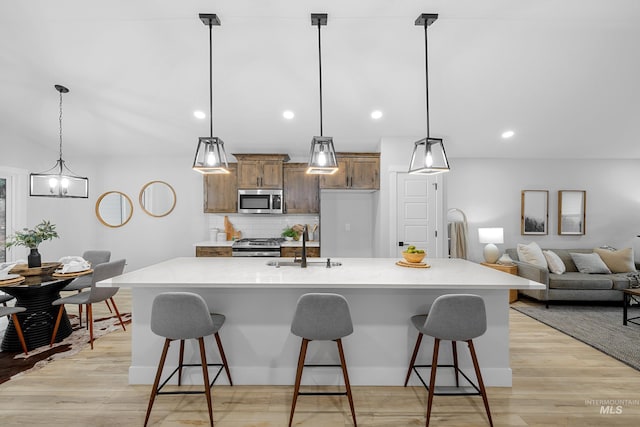 kitchen featuring light wood-type flooring, appliances with stainless steel finishes, a large island, hanging light fixtures, and decorative backsplash