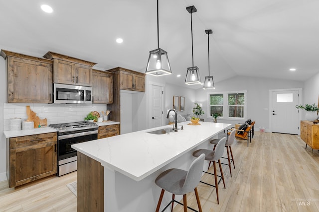 kitchen with stainless steel appliances, hanging light fixtures, sink, an island with sink, and light hardwood / wood-style flooring