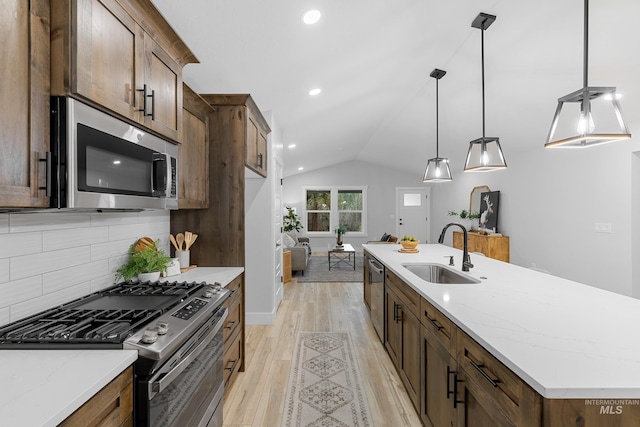 kitchen featuring lofted ceiling, sink, light wood-type flooring, appliances with stainless steel finishes, and decorative light fixtures