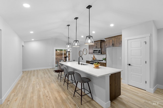 kitchen featuring light hardwood / wood-style floors, a center island with sink, sink, appliances with stainless steel finishes, and pendant lighting