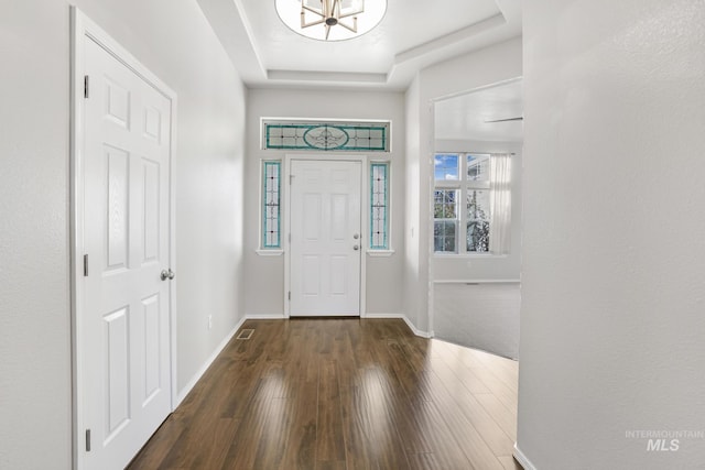 foyer with a tray ceiling, a notable chandelier, wood finished floors, baseboards, and visible vents