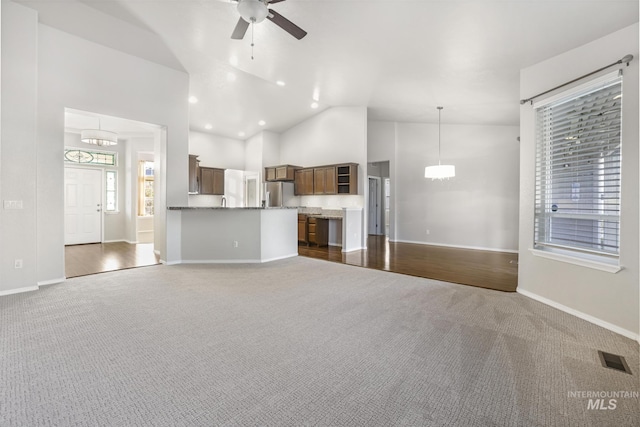 unfurnished living room with high vaulted ceiling, visible vents, baseboards, ceiling fan with notable chandelier, and dark colored carpet