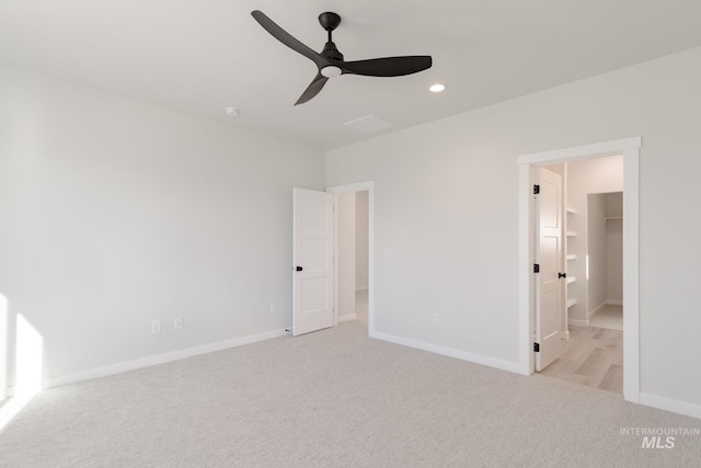 unfurnished bedroom with baseboards, recessed lighting, a walk in closet, and light colored carpet