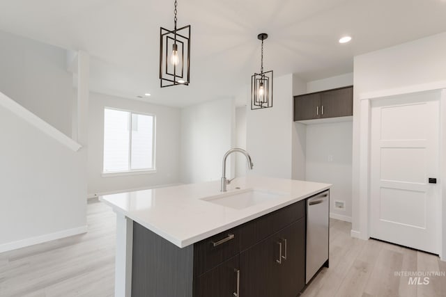 kitchen featuring light wood-style flooring, a sink, light countertops, stainless steel dishwasher, and pendant lighting