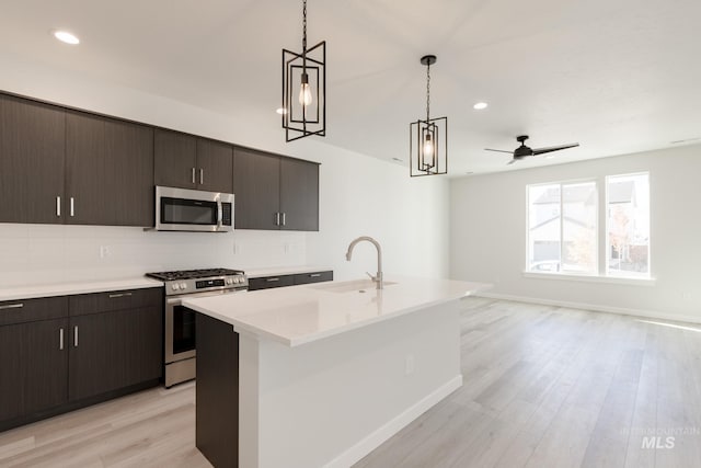 kitchen with light wood finished floors, a sink, light countertops, stainless steel appliances, and backsplash