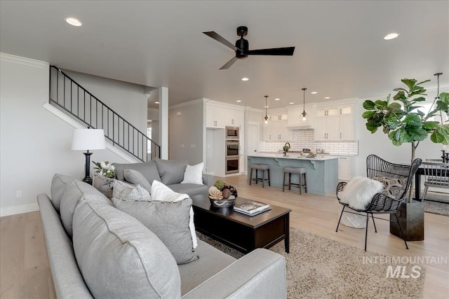 living room with ceiling fan, sink, light hardwood / wood-style floors, and ornamental molding