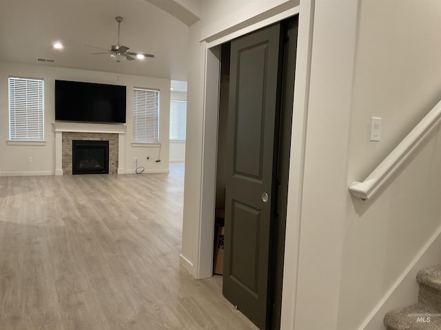 interior space with a ceiling fan, baseboards, light wood-style flooring, a fireplace, and stairs