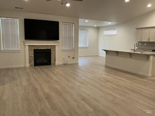 unfurnished living room with visible vents, light wood-style flooring, a fireplace, a ceiling fan, and a sink