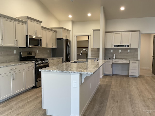 kitchen featuring a kitchen island with sink, a sink, stainless steel appliances, light wood-style floors, and light stone countertops