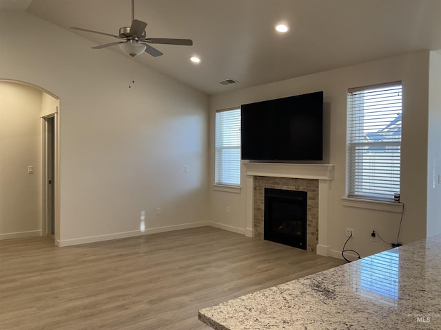 unfurnished living room with visible vents, lofted ceiling, a fireplace, arched walkways, and light wood-style floors