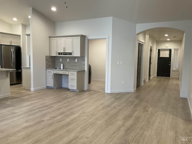 kitchen featuring arched walkways, light wood finished floors, tasteful backsplash, and freestanding refrigerator