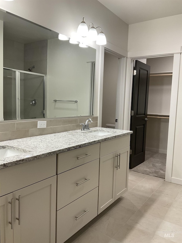 bathroom with a shower stall, double vanity, a chandelier, and a sink