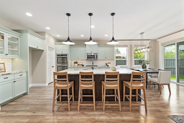 5404 S Palatino Ave, Meridian, ID 83642 - kitchen with appliances with stainless steel finishes, tasteful backsplash, light wood finished floors, a kitchen island with sink, and recessed lighting