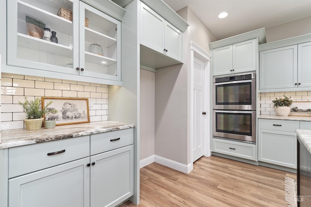 5404 S Palatino Ave, Meridian, ID 83642 - kitchen with stainless steel double oven, tasteful backsplash, glass insert cabinets, light wood-style flooring, and light stone countertops