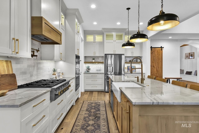kitchen featuring appliances with stainless steel finishes, a barn door, a sink, a large island with sink, and recessed lighting