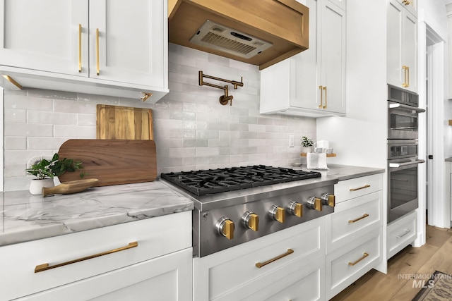 kitchen with stainless steel appliances, white cabinets, decorative backsplash, and range hood