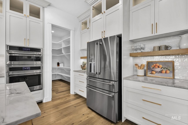 kitchen with appliances with stainless steel finishes, light stone counters, light wood-style floors, and white cabinets