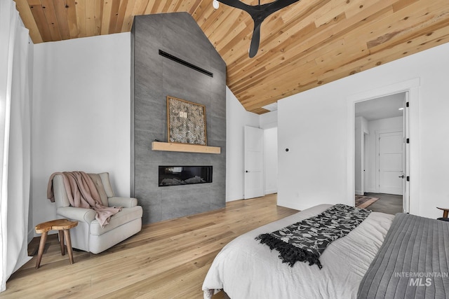 bedroom featuring wood ceiling, wood finished floors, a tiled fireplace, and high vaulted ceiling